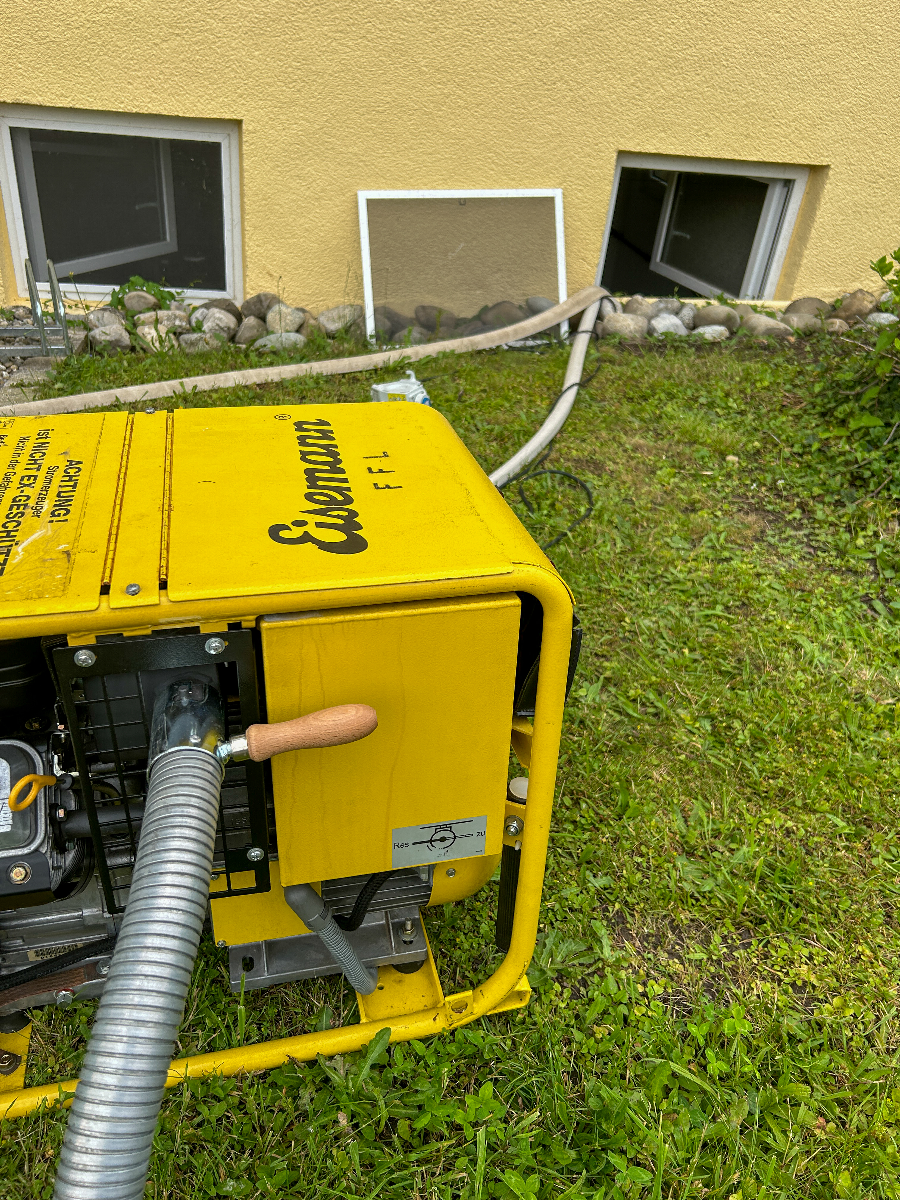 Zu sehen ist wie der Stromerzeuger vor einem Kellerfenster steht aus dem gerade Wasser gepumpt wird.