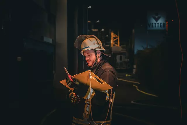 Ein Feuerwehrmann steht vor einem Gebäude. Inder Hand hält er ein Tableau zur Atemschutzüberwachung. Im Hintergrund ist das Logo der Firma Vetter an einer Hallenfassade erkennbar.