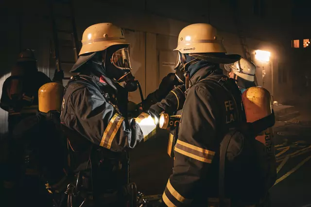 Zwei Feuerwehrmänner unter Atemschutz bereiten sich gegenseitig für den Einsatz vor. 