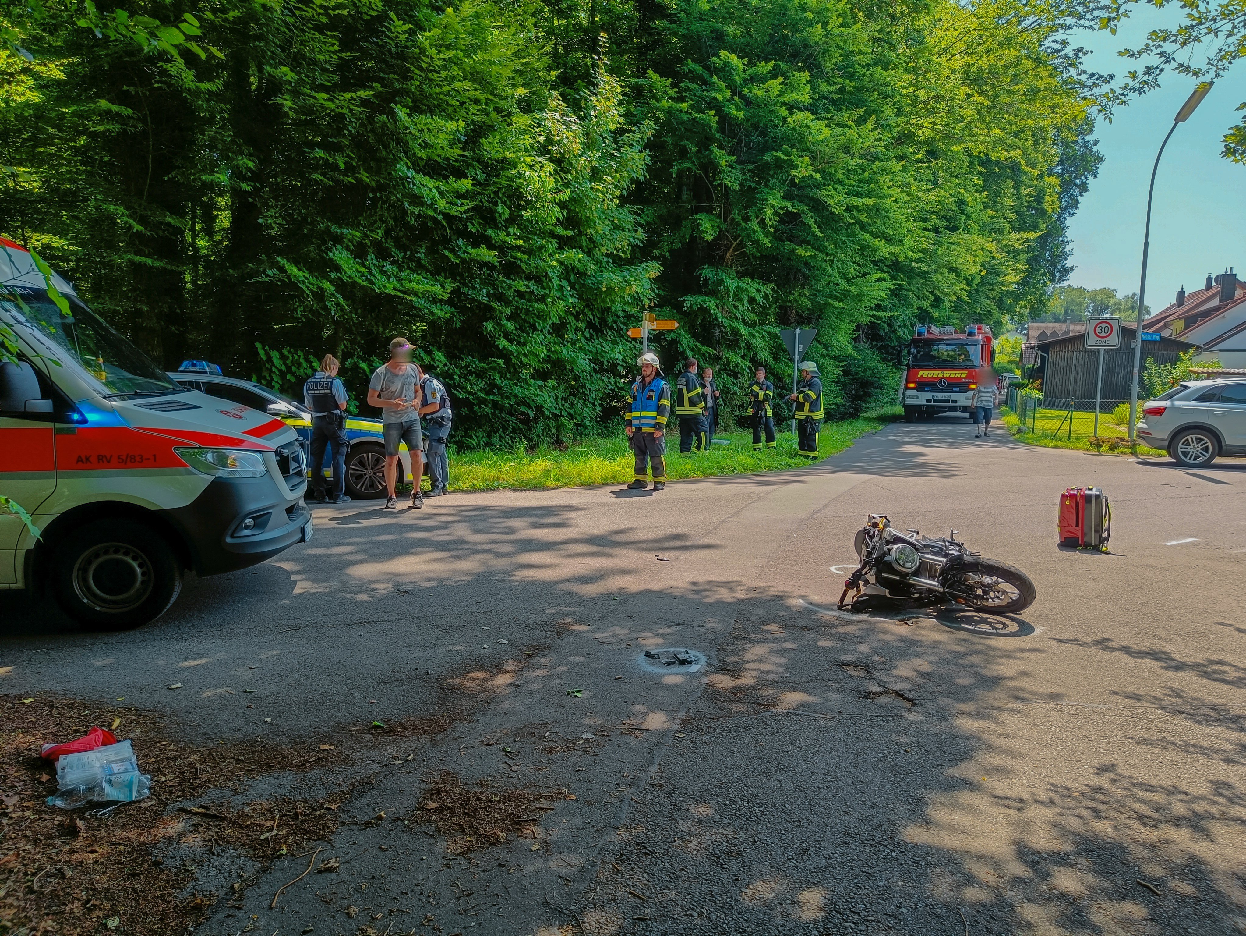 Ein Motorrad liegt auf der Straße, links daneben ist ein Rettungswagen der Johanniter zu sehen. Mehrere Personen stehen auf der Straße