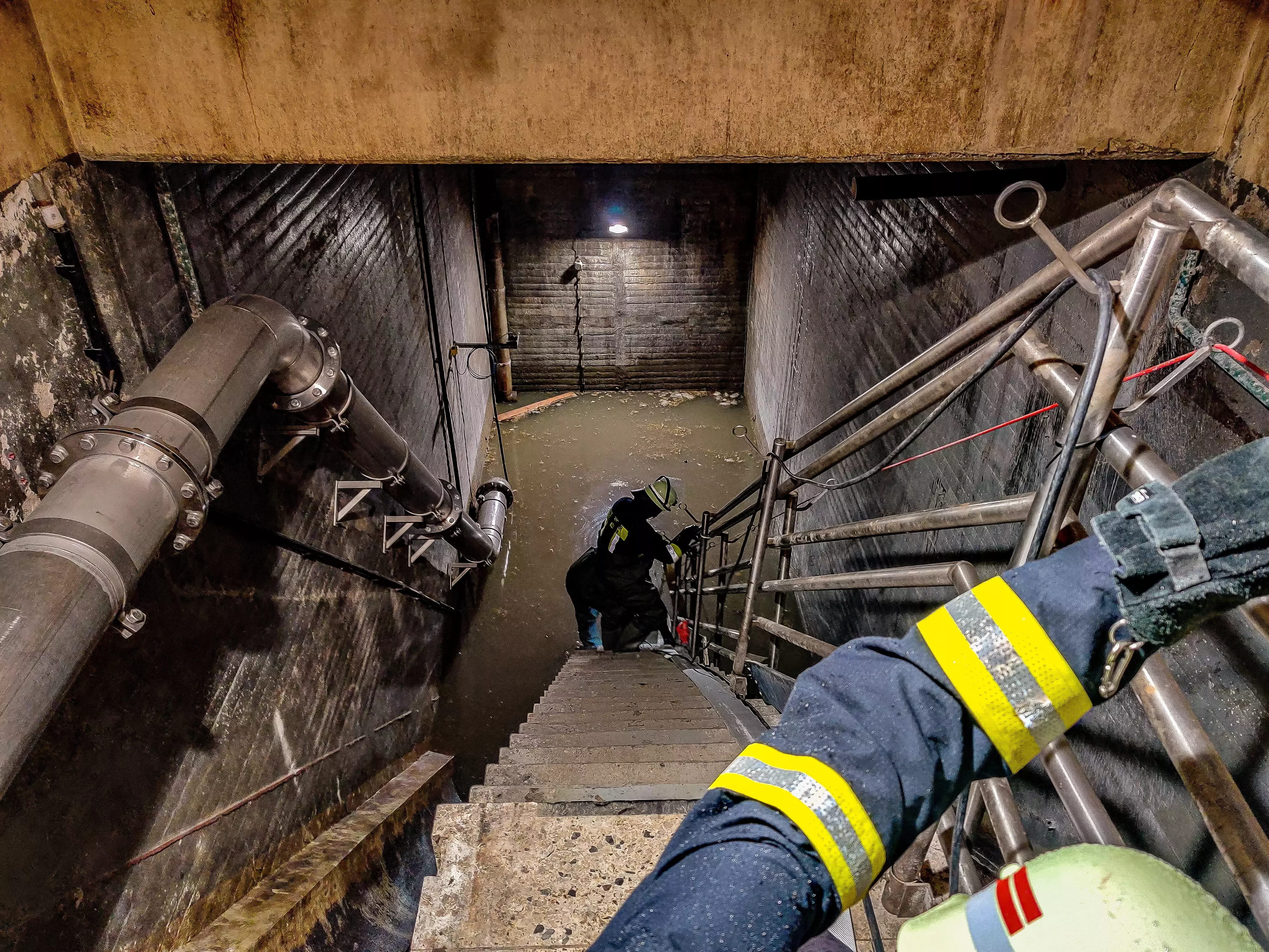 Zwei Feuerwehrmänner sind am Ende der Treppe zu sehen, wie sie eine Tauchpumpe vornehmen, um Wasser abzupumpen.