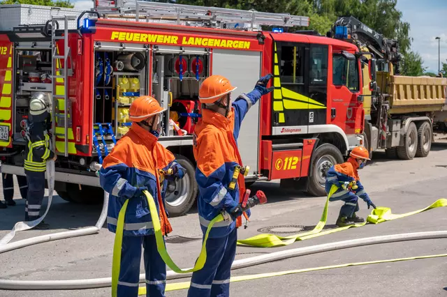 Im Vordergrund hat ein Trupp den Löschangriff vorbereitet und gibt den Befehl Wasser Marsch. Im Hintergrund steht das Löschfahrzeug 10 aus Langenargen mit Blaulicht.