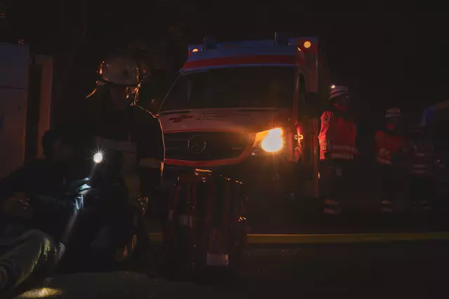 Eine Feuerwehrfrau stützt einen Verletztendarsteller. Der Lichtkegel ihrer Handlampe fällt vor ihr auf den Boden. Im Hintergrund ist ein Rettungswagen des DRK und mehrere Sanitäter zu sehen.