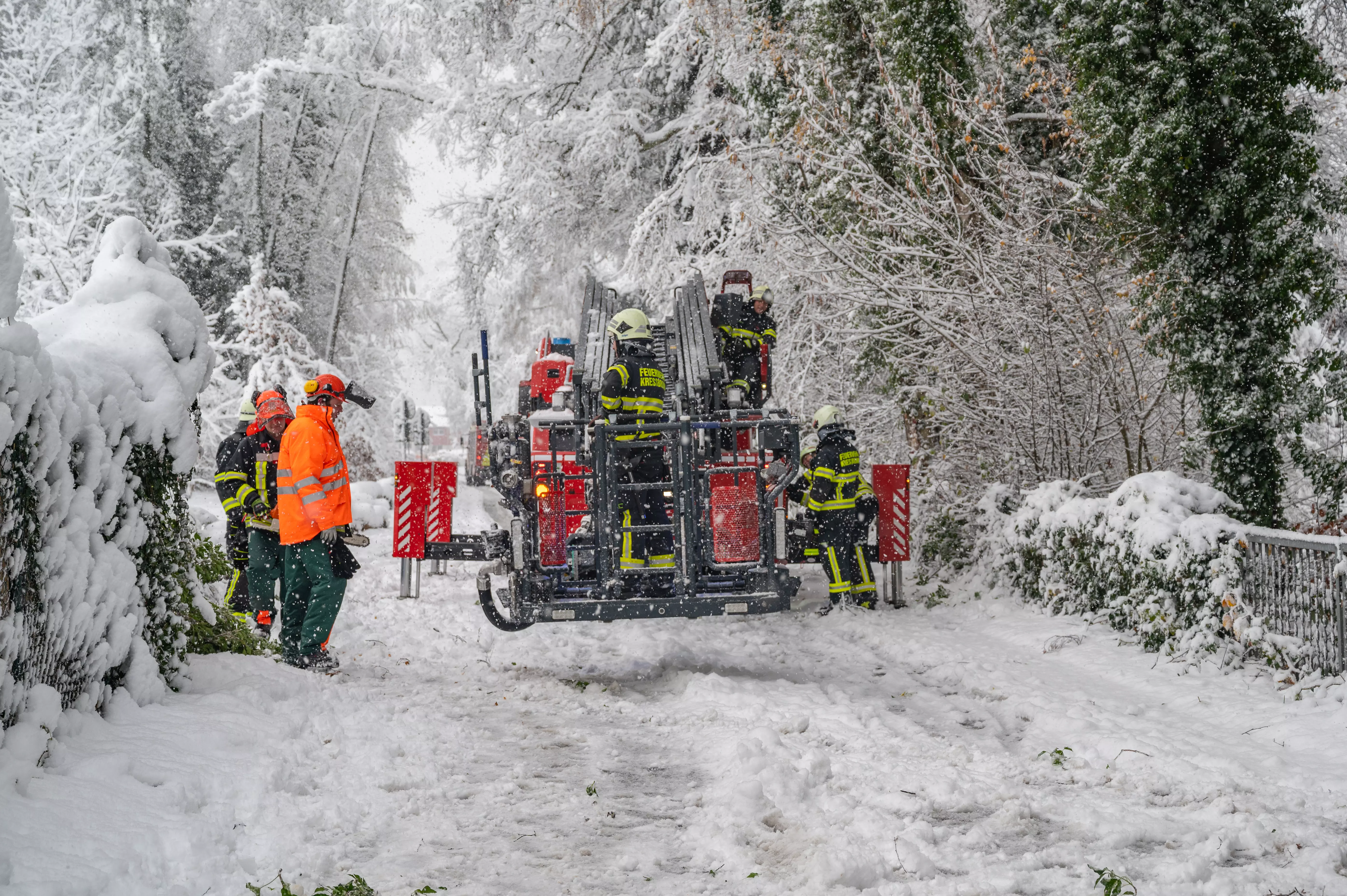 Feuerwehrleute stehen auf der Straße und im Korb einer Drehleiter und bereiten sich auf ihren Einsatz vor.