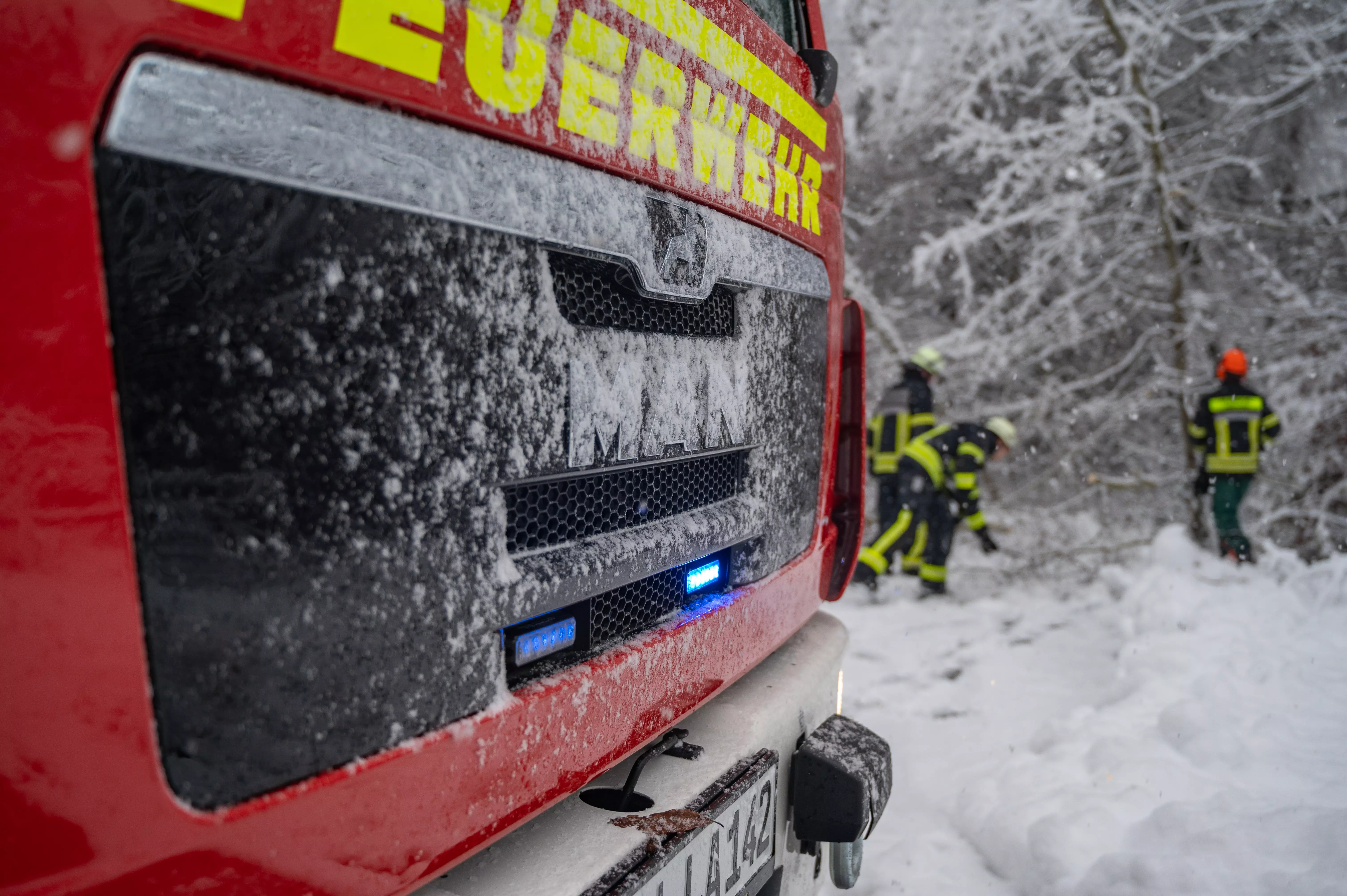 Löschfahrzeug mit Blaulicht. Im Hintergrund entfernen Einsatzkräfte Bäume und Äste