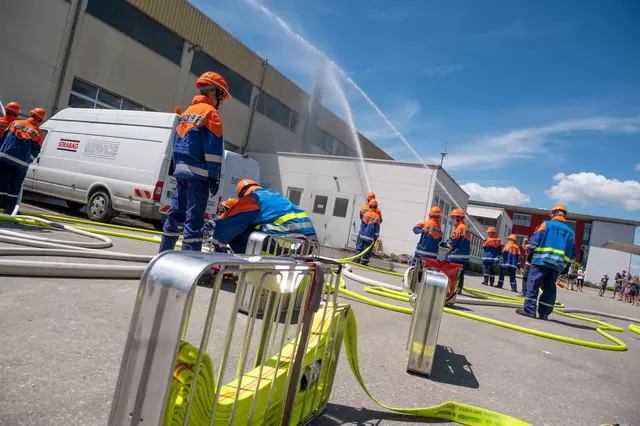 Im Vordergrund ein Schlauchtragekorb. Im Hintergrund mehrere Jutendfeuerwehrler, die aus Strahlrohren den fiktiven Brand löschen.