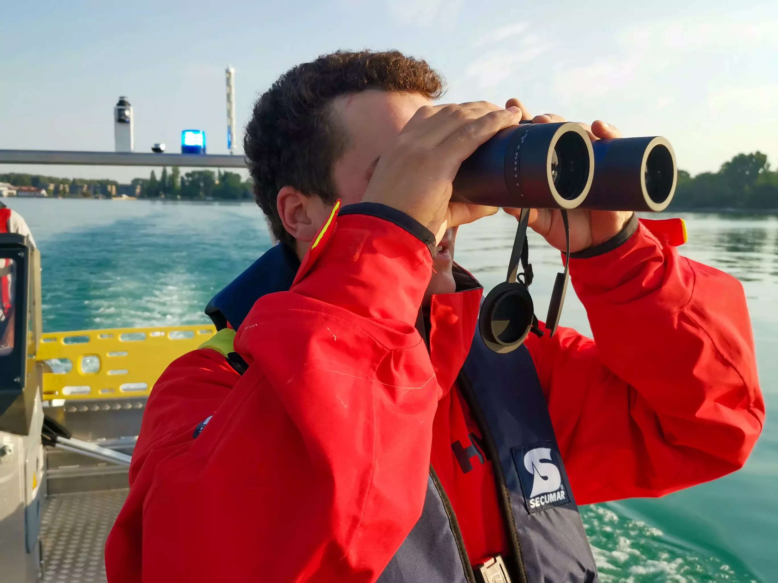 Durch ein Fernglas sucht ein Feuerwehrmann von Bord des MZB 1 den See nach einer vermissten Person ab.