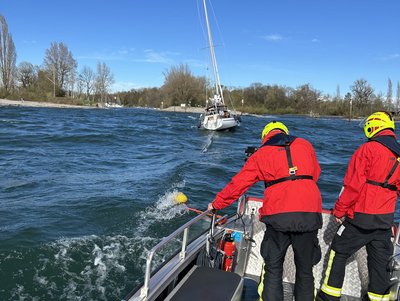 Zu sehen ist wie der Havarist von der DLRG und der Feuerwehr in den Hafen geschleppt wird.