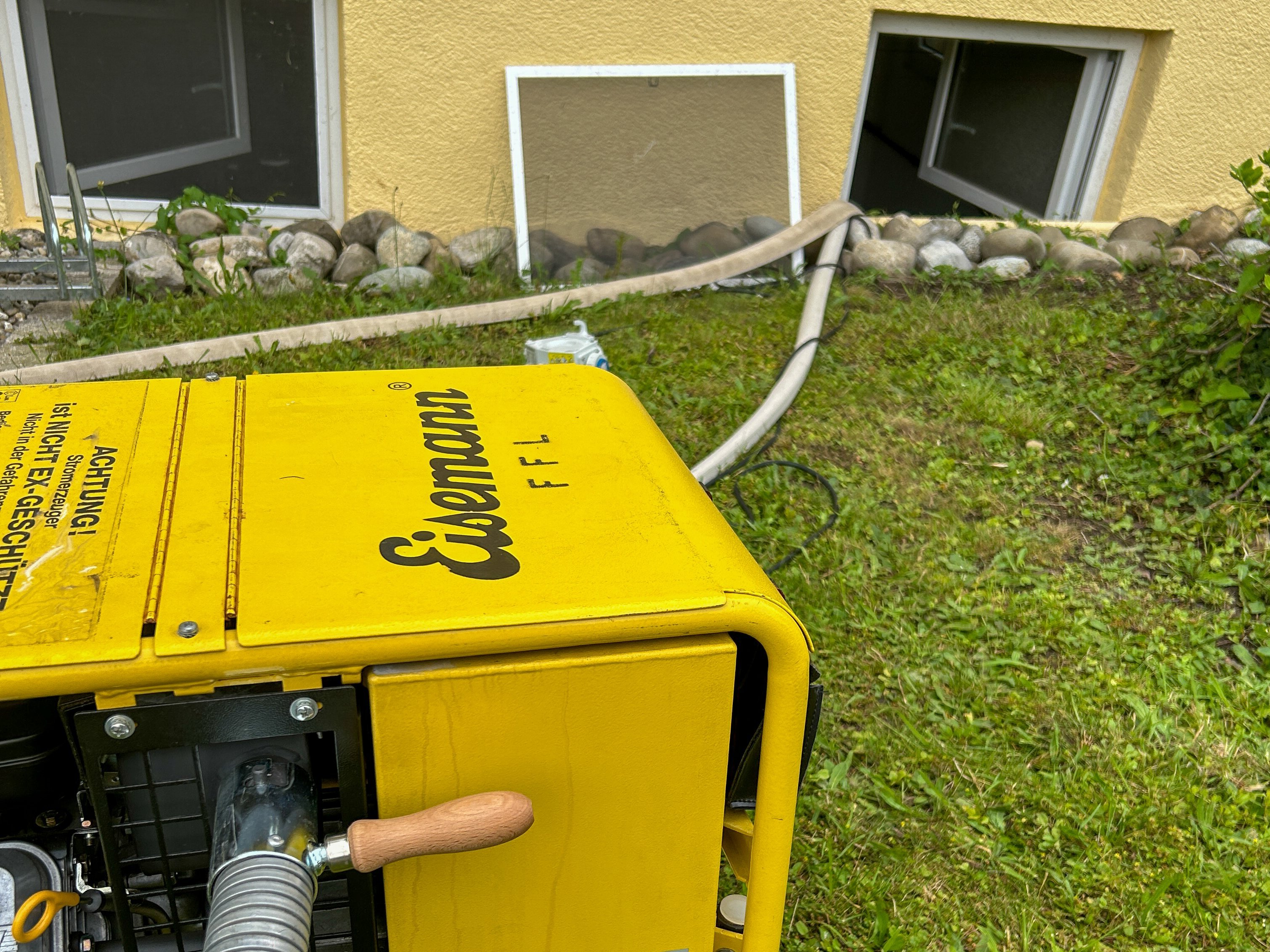 Zu sehen ist wie der Stromerzeuger vor einem Kellerfenster steht aus dem gerade Wasser gepumpt wird.