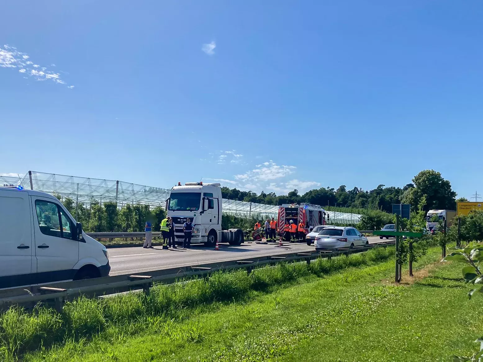 Fließender Verkehr auf der Bundesstraße. Im Hintergrund eine Zugmaschine eines Sattelschleppers, daneben ein Löschfahrzeug der Feuerwehr Kressbronn.