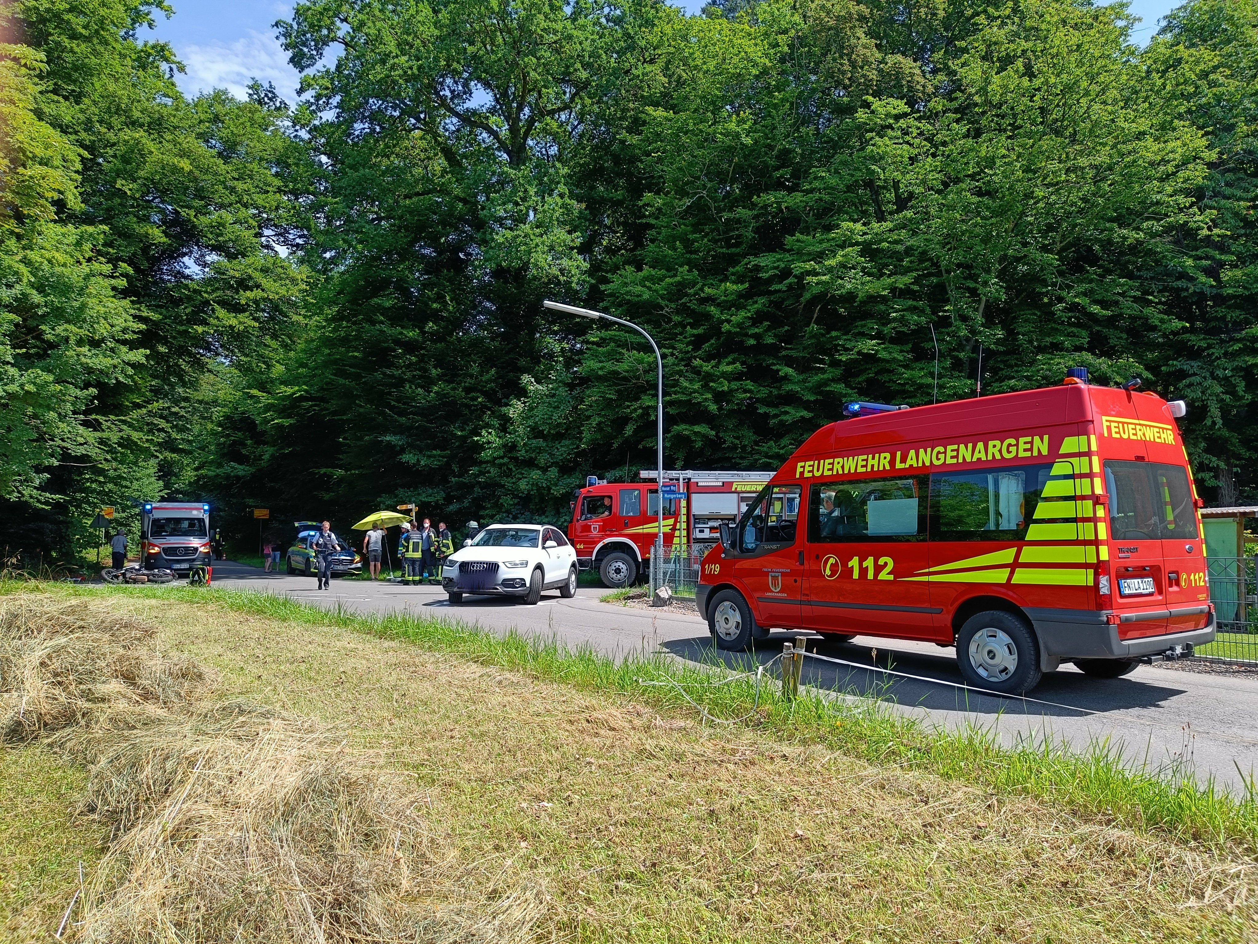 Im Vordergrund steht der MTW 1 der Feuerwehr Langenargen, im Hintergrund ist der Unfall-PKW und die Unfallstelle zu sehen. Es handelt sich um eine Kreuzung am Waldrand