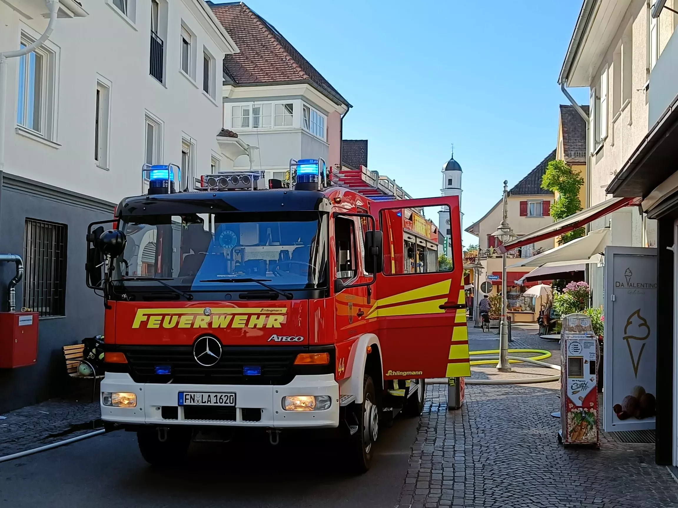 Das Löschfahrzeug 16 steht mit Blaulicht auf einer Straße im Ortskern von Langenargen.