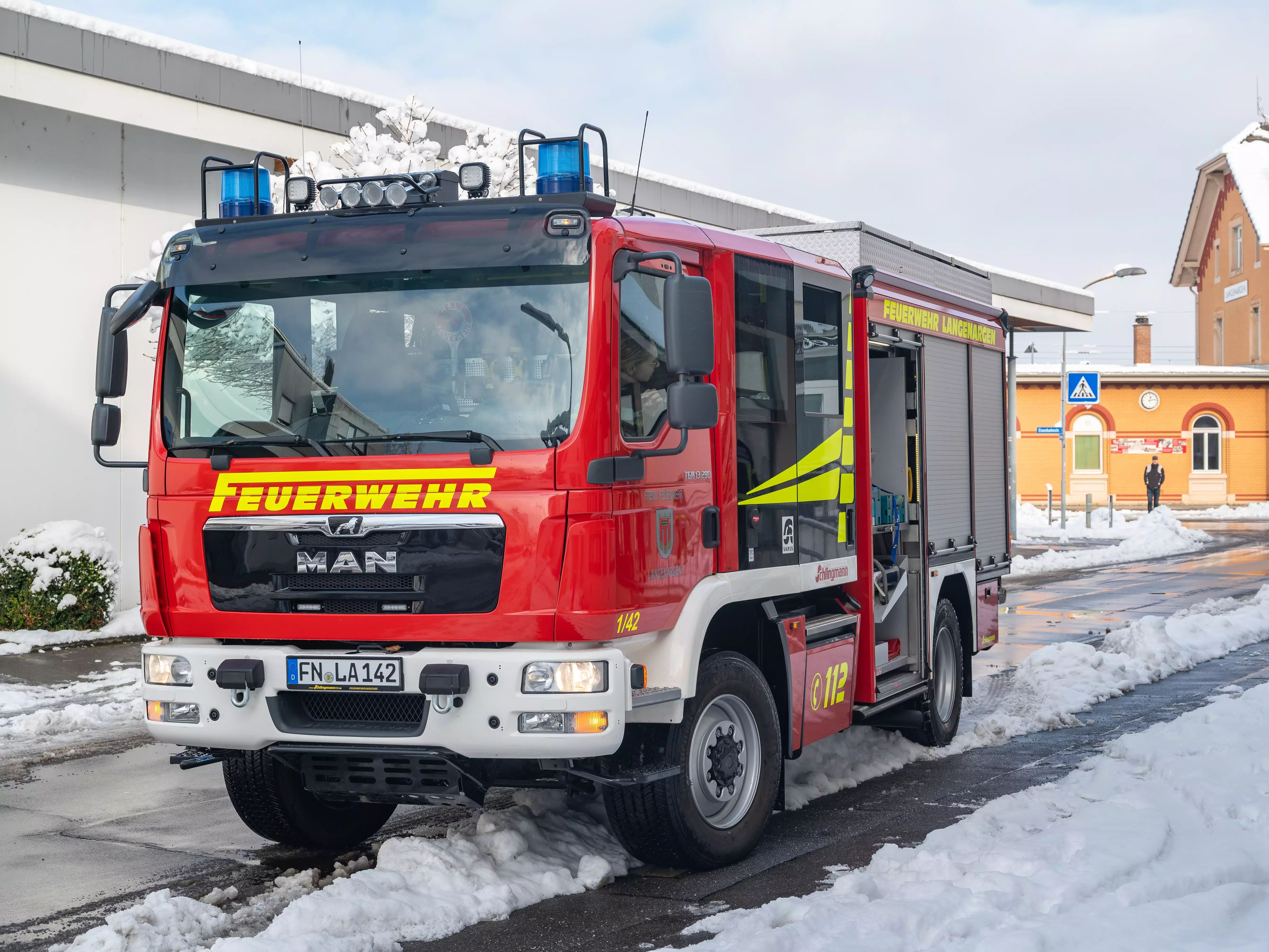 Das Löschfahrzeug 1/42 steht auf einer Straße. Im Hintergrund ist der Bahnhof zu sehen.